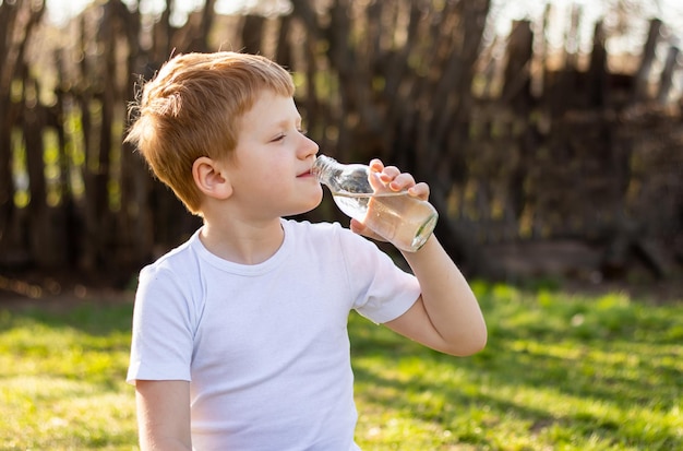 Roodharige tienerjongen in witte tshirt mediteren in de natuur doen yoga rustend drinkwater