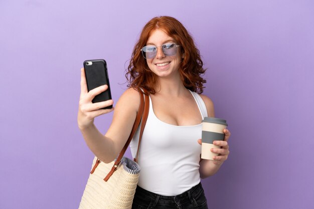 Roodharige tienermeisje met een strandtas geïsoleerd op een paarse achtergrond met koffie om mee te nemen en een mobiel