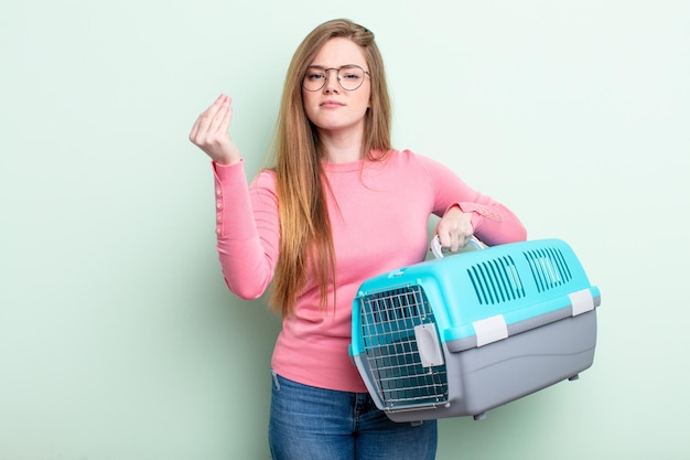 Roodharige vrouw die capice of geldgebaar maakt en zegt dat je moet betalen reis huisdier vervoerder concept