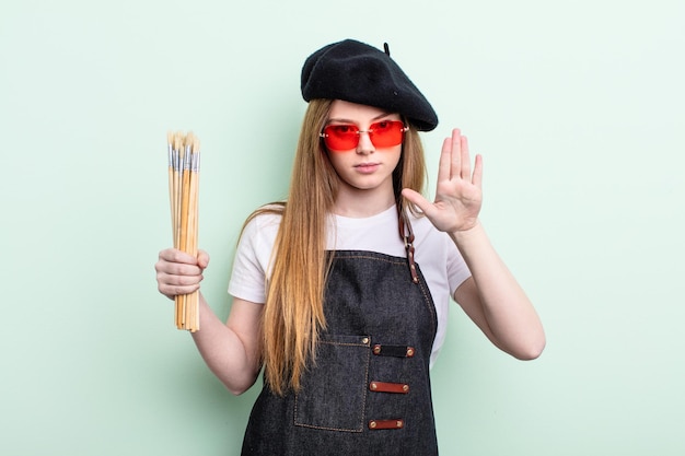 Roodharige vrouw die er serieus uitziet met open palm die het concept van de artiest van het stopgebaar maakt