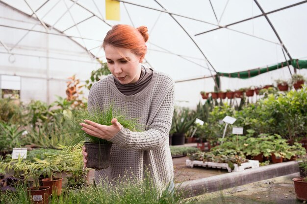 Roodharige vrouw die kamerplanten kiest in de kas van het tuincentrum