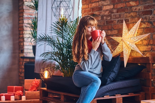 Roodharige vrouw drinkt een warme koffie in een woonkamer met loft interieur.