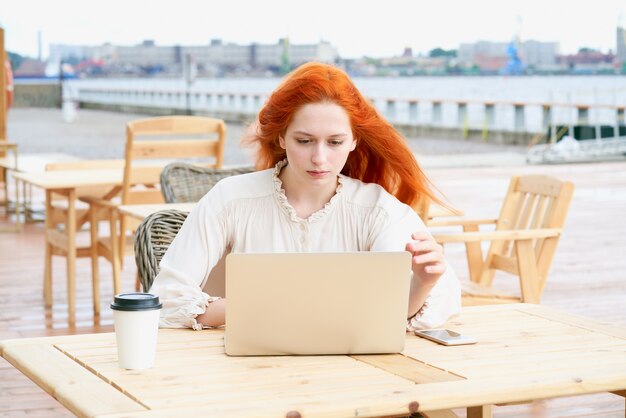 Roodharige vrouw kijken naar laptop in café buiten