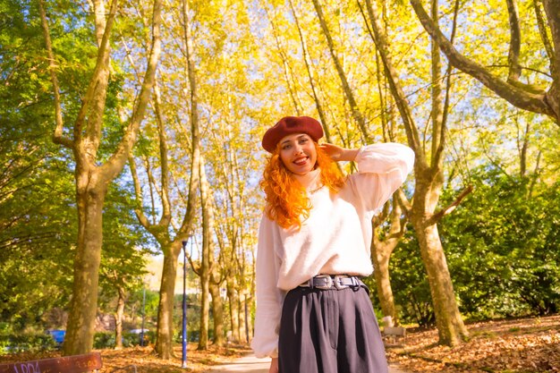 Roodharige vrouw met baret in een park stadsbos bij zonsondergang glimlachen