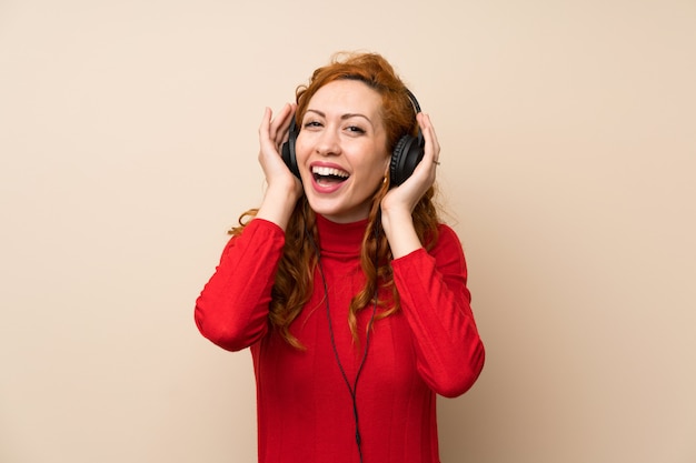 Roodharige vrouw met coltrui trui luisteren naar muziek met een koptelefoon