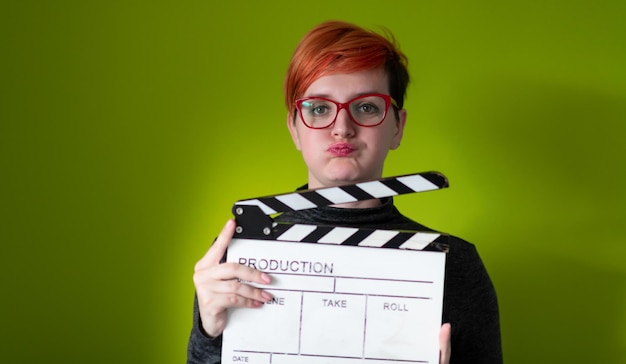 roodharige vrouw met film klepel geïsoleerd tegen groene achtergrond bioscoop concept in studio