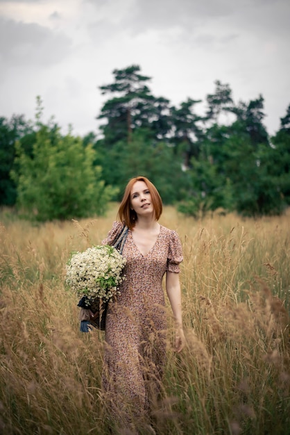 Roodharige vrouw van veertig jaar met een groot boeket wilde bloemen in de zomer in de natuur