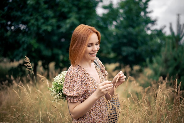 Roodharige vrouw van veertig jaar met een groot boeket wilde bloemen in de zomer in de natuur