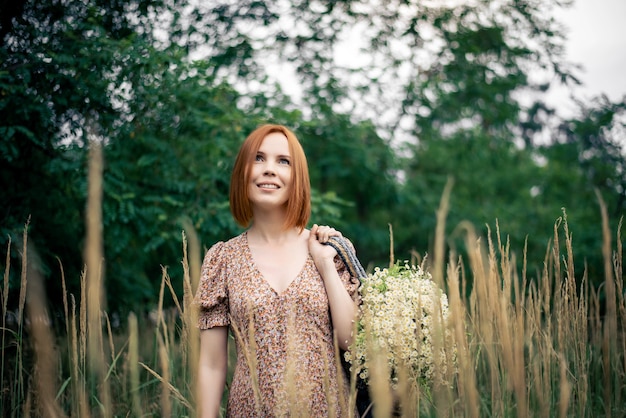 Roodharige vrouw van veertig jaar met een groot boeket wilde bloemen in de zomer in de natuur