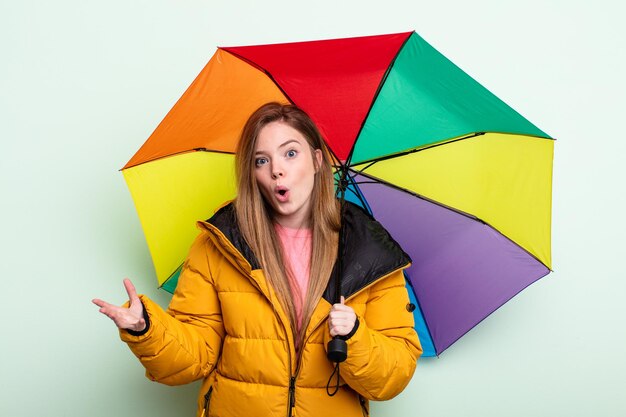 Roodharige vrouw verbaasd, geschokt en verbaasd met een ongelooflijke verrassing. paraplu concept