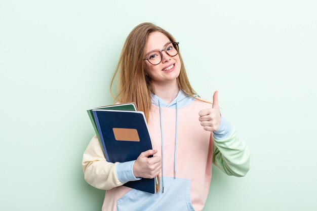 Roodharige vrouw voelt zich trots, positief glimlachend met duimen omhoog. studentenconcept