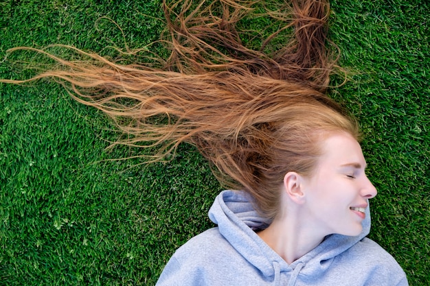 Roodharige witte jonge vrouw die en op het gazon van voetbalgebied liggen ontspannen.