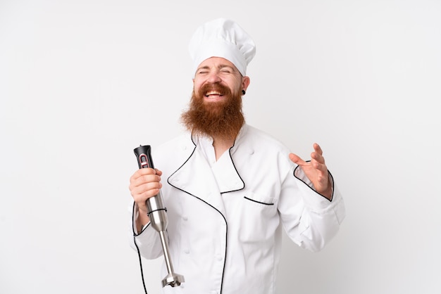 Roodharigemens die handmixer over het geïsoleerde witte muur lachen gebruiken