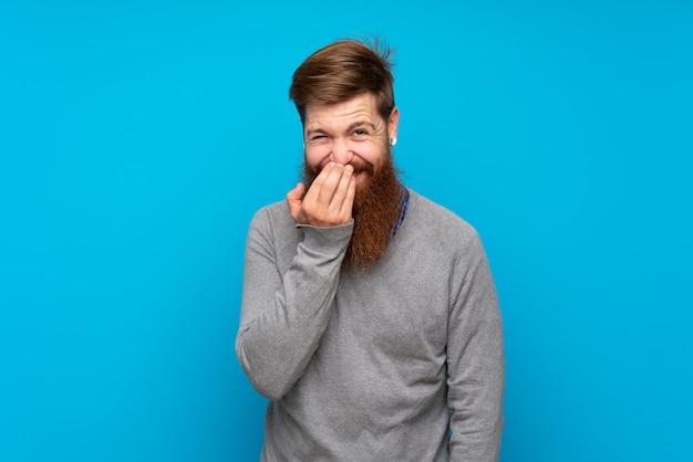 Roodharigemens met lange baard over blauwe muur die veel glimlacht