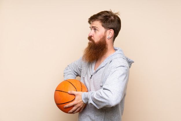 Roodharigemens met lange baard over geïsoleerde muur met bal van basketbal