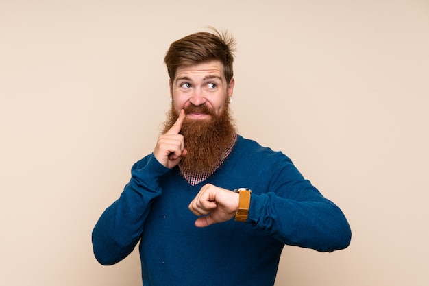 Roodharigemens met lange baard over geïsoleerde muur met polshorloge en het denken van een idee