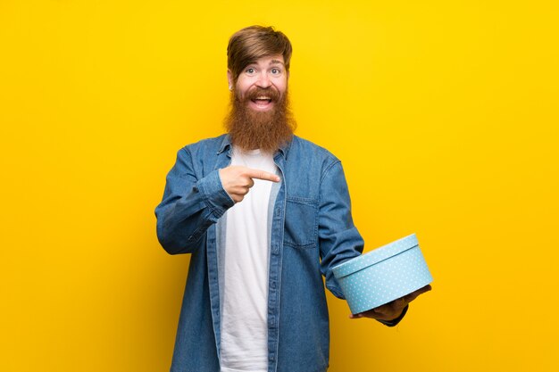 Roodharigemens met lange baard over gele de giftdoos van de muurholding