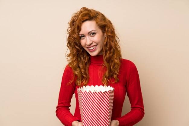 Roodharigevrouw die met coltrui een kom popcorns houden