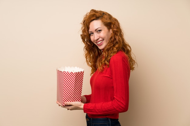 Roodharigevrouw die met coltrui een kom popcorns houden