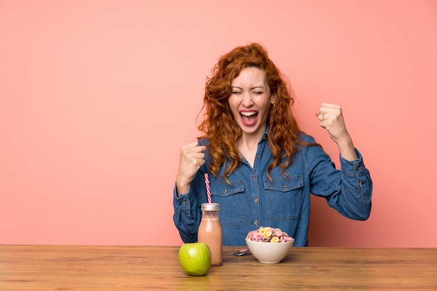 Roodharigevrouw die ontbijtgraangewassen en fruit hebben die een overwinning vieren