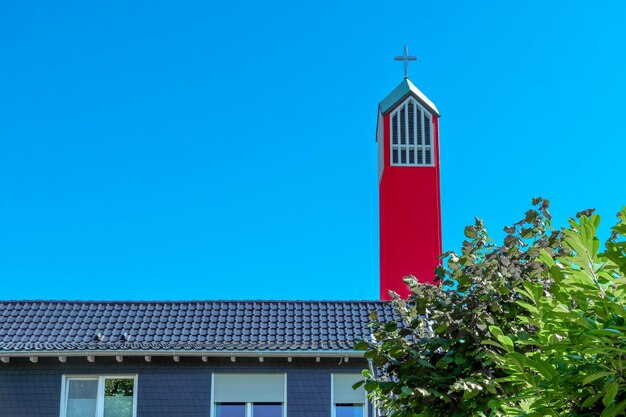 Foto tetto di una chiesa cristiana con una torre rossa e una croce su alberi verdi contro un cielo blu con nuvole