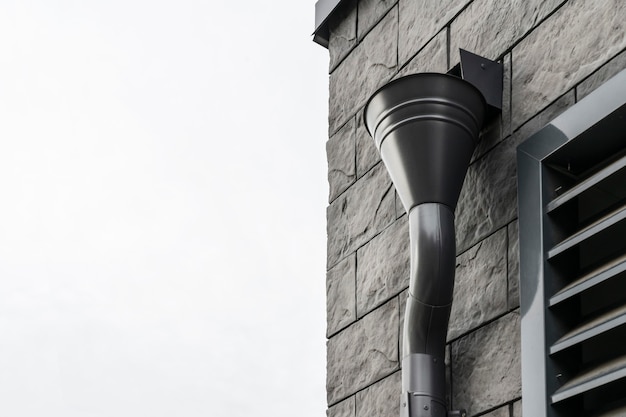 Roof gutter mounted on the wall of the building lined with modern stone tiles black and brown stylish color modern design element closeup