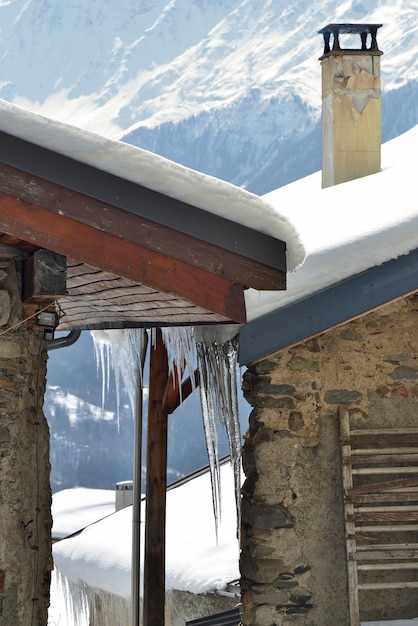 Roof of house in alpine village covered with snow and icicles