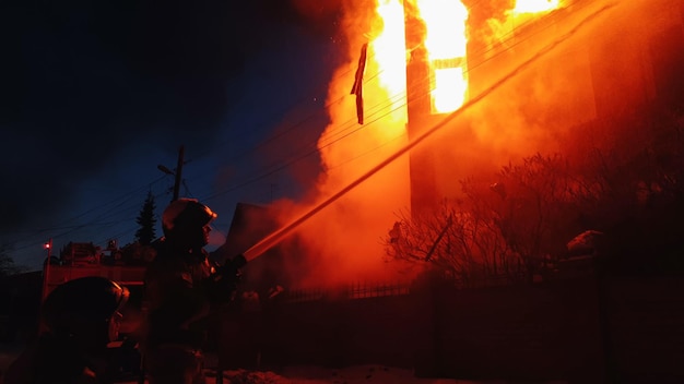 The roof of the house is on fire. The residential building burn, village. Firefighters put out a fire from the crane from above. Smoke and sparks.