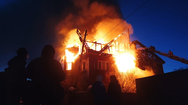 The roof of the house is on fire. The residential building burn, village. Firefighters put out a fire from the crane from above. Smoke and sparks.