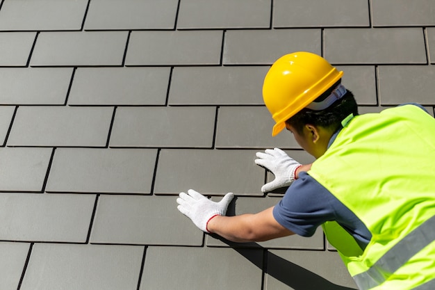 Photo roof repair, worker with white gloves replacing gray tiles or shingles on house with blue