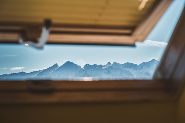 Roof window view of sunset in the mountains view from the attic\
window of the wooden cottage in mountain valley panorama of snowy\
mountains