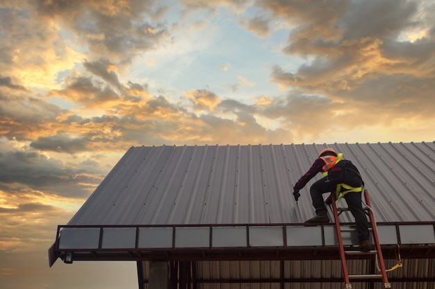 Roofer 건설 노동자는 새 지붕, 지붕 도구, 금속 시트로 새 지붕에 사용되는 전기 드릴을 설치합니다.