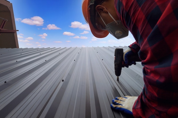 写真 屋根葺き職人の建設作業員は、新しい屋根、屋根ふきツール、金属シートを使用して新しい屋根に使用される電気ドリルを設置します。
