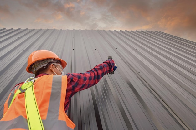 사진 roofer 건설 노동자는 새 지붕, 지붕 도구, 금속 시트로 새 지붕에 사용되는 전기 드릴을 설치합니다.