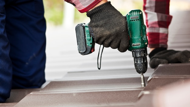 roofer worker screwing metal tile on roof