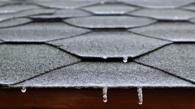 Copertura del tetto di una casa o gazebo in tegole bituminose con acqua corrente ghiacciata e ghiaccioli appesi. avvicinamento.