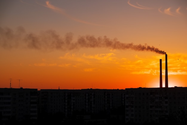 Roofs of city houses during sunset. Dark smoke coming from the thermal power plant pipe.