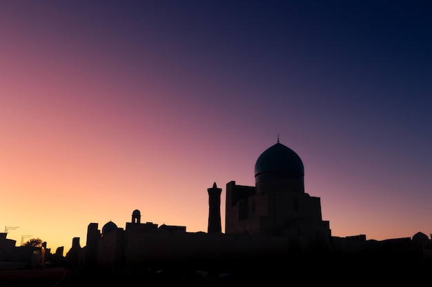 Rooftop silhouette with old mosque big dome against colorful sunset sky Bukhara Uzbekistan