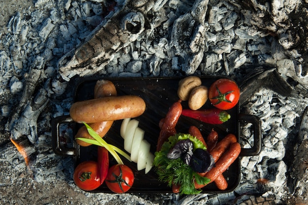 Rookworsten en tomaten liggen op houtskool. het gerecht wordt gekookt en gerookt op houtskool