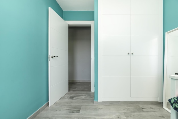 A room in a builtin closet with white wooden doors and turquoise blue walls