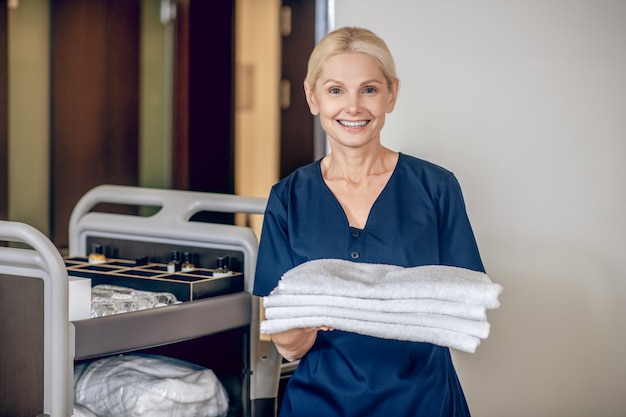 Room cleaning. Service woman in a protective mask with a trolley carrying clean towels