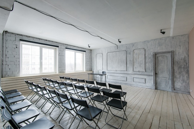 Room for lecture with a lot of dark chairs. Walls are white, loft interior. On the right there is  door.