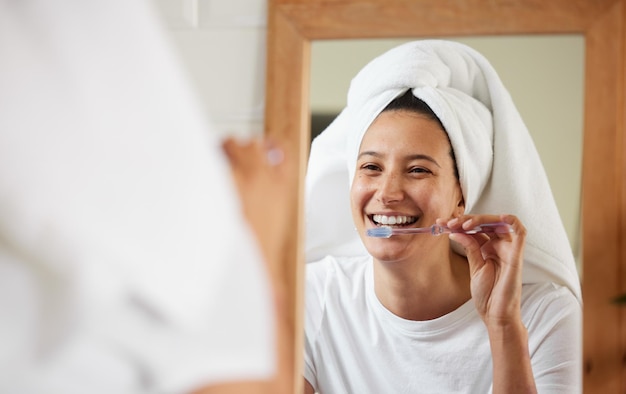 Комната буквально светится, когда она улыбается. Снимок: молодая женщина чистит зубы, глядя в зеркало в ванной.