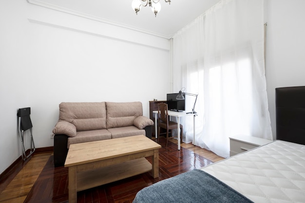 Room with bed and sofa bed white study table coffee table and varnished oak parquet floors