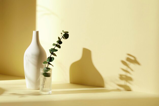 Photo a room with various objects such as warm sunlight shadows of grass leaves a vase on a table and c