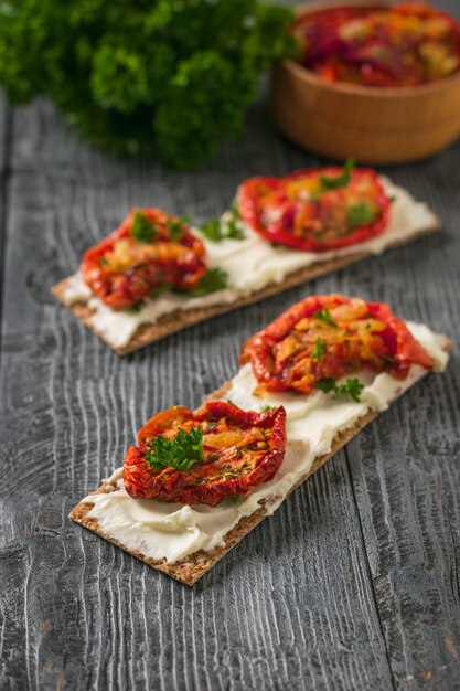 Roomkaas en zongedroogde tomaten op broodtoost op een houten lijst. vegetarische snack van kwark en tomaten.