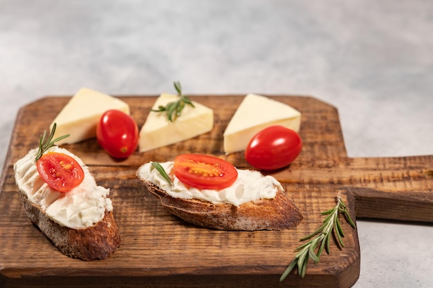 Roomkaas sandwiches met tomaat en rozemarijn op bruin houten bord, vrije ruimte voor tekst. Hoge kwaliteit foto