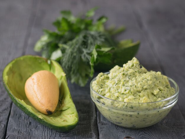 Roompuree avocado met peterselie, dille en knoflook in een kom op een vintage tafel. Het gerecht is vegetarisch dieet.