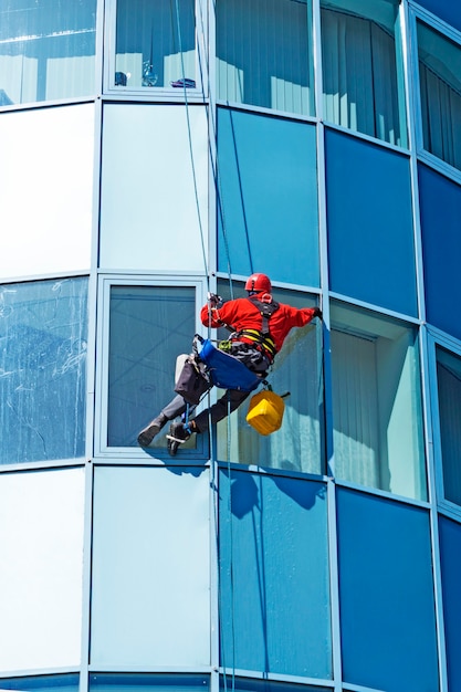 Rope access technician in a helmet washes the window of a\
highrise building from the outside