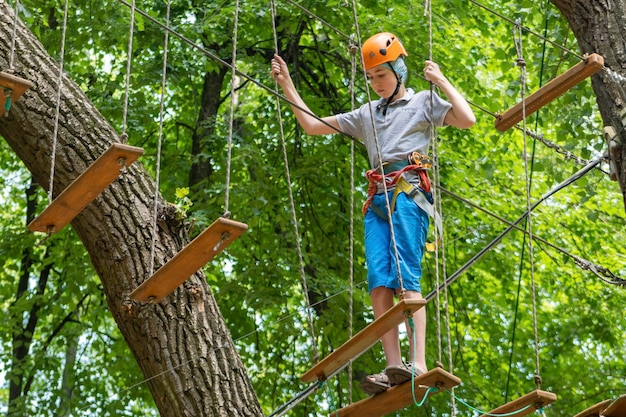 Rope park A boy teenager in a helmet walks on suspended rope ladders Carabiners and safety straps Safety Summer activity Sport Children's playground in nature in the forest
